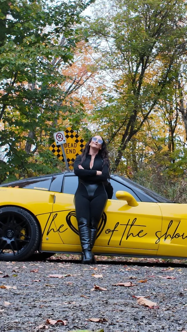 Chelsea with arms crossed in front of the Corvette.