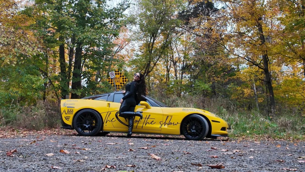 Chelsea leaning playfully against the side of the yellow Corvette.