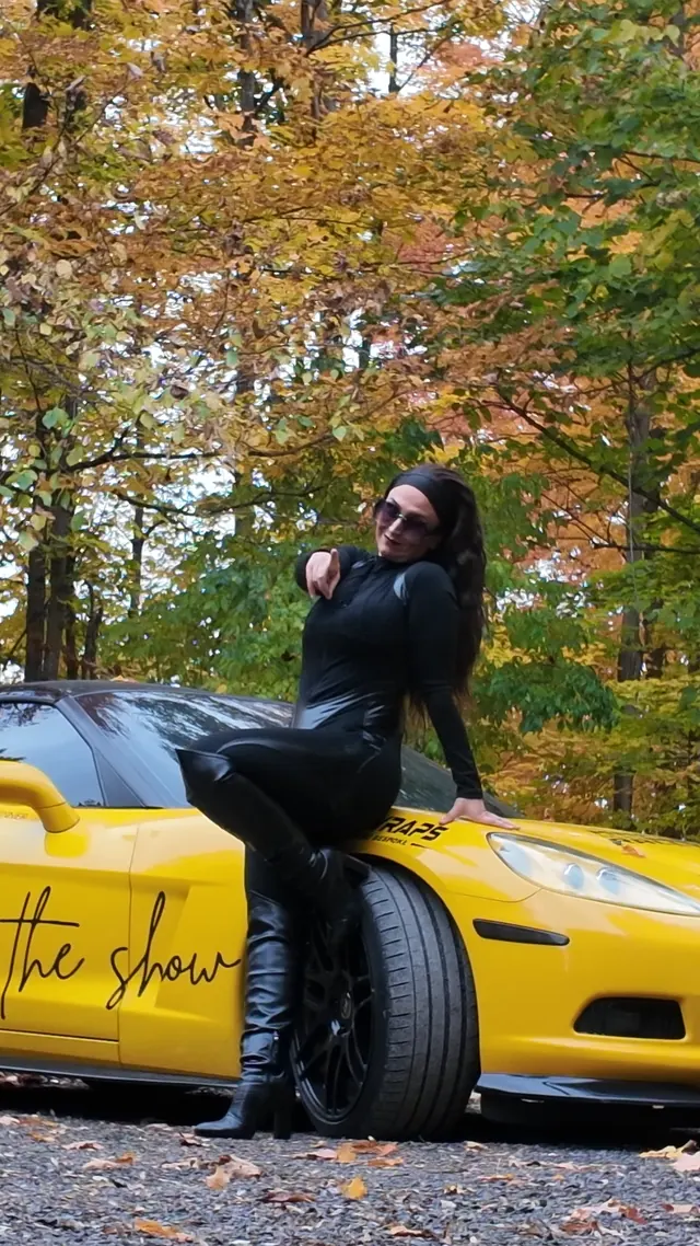Chelsea pointing toward the camera from the Corvette's fender.
